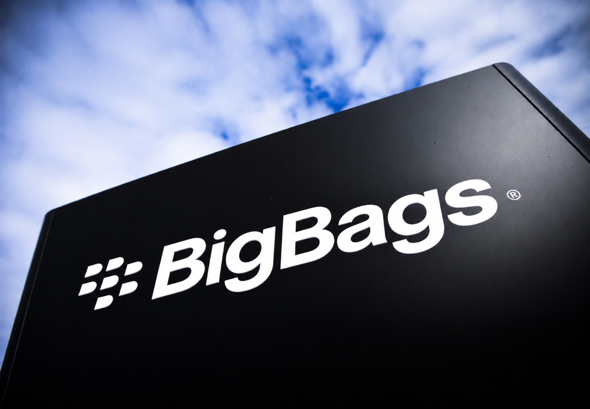 A BigBags monolith sign against a bright, cloud-streaked sky.